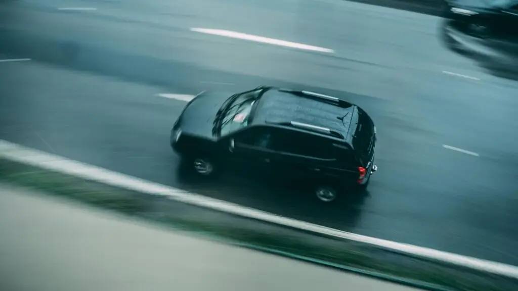 Blurred motion of a black SUV speeding on a wet highway, capturing a sense of motion.