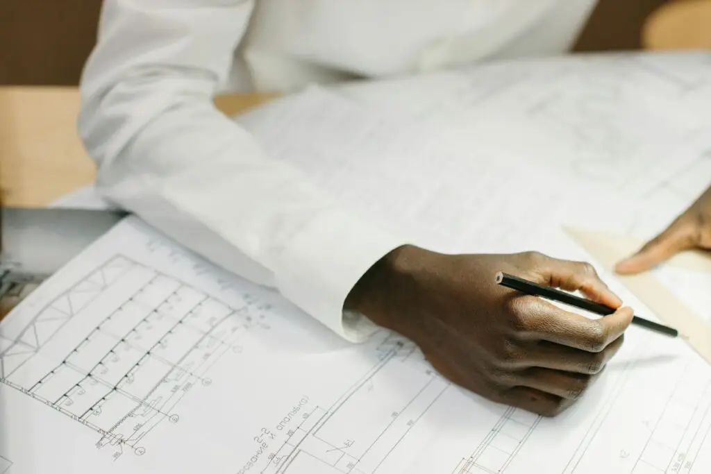 Architect working on detailed floor plans with a pencil and set square, captured in bright indoor setting.